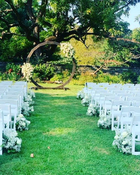 Lawn ceremony with white chairs and a round arch under a large tree