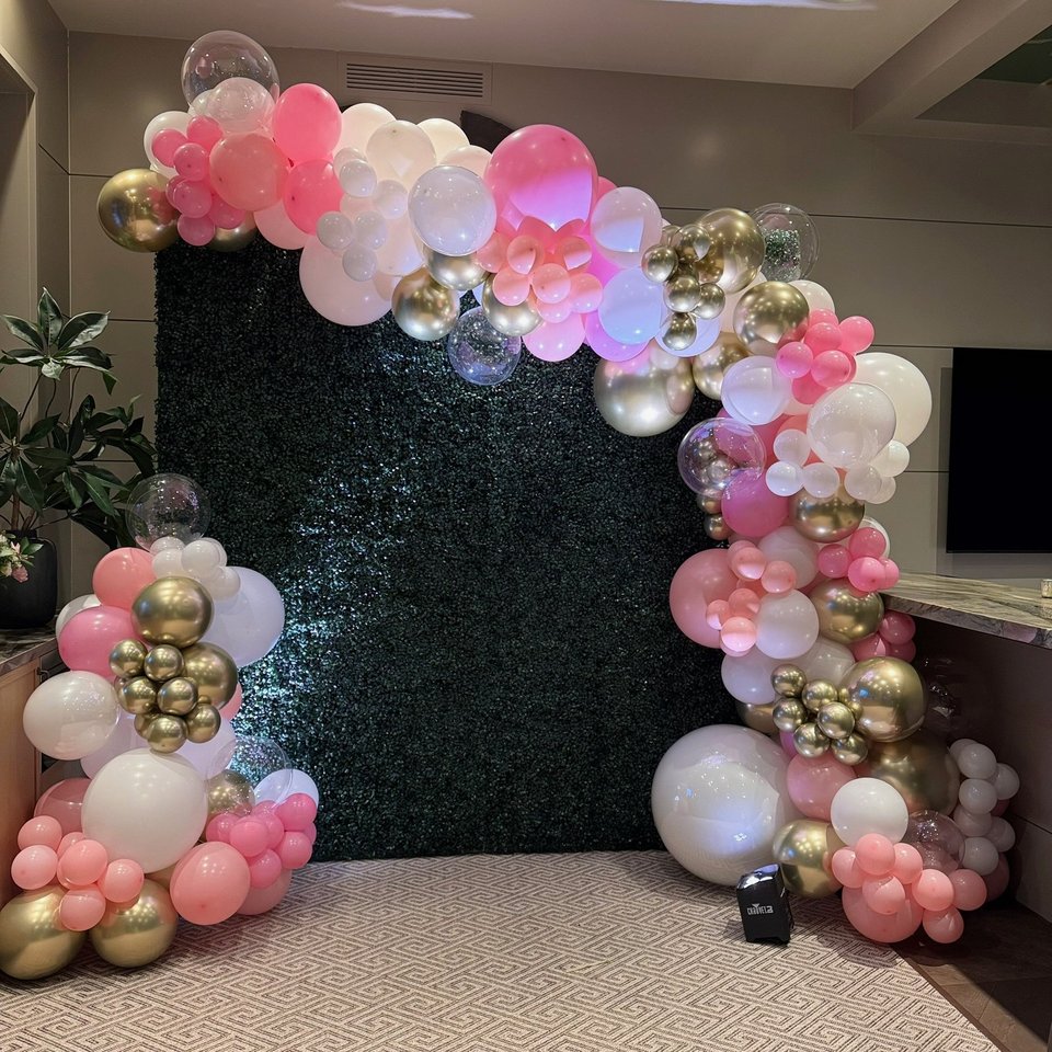 Pink, white, and gold balloon garland around a greenery wall