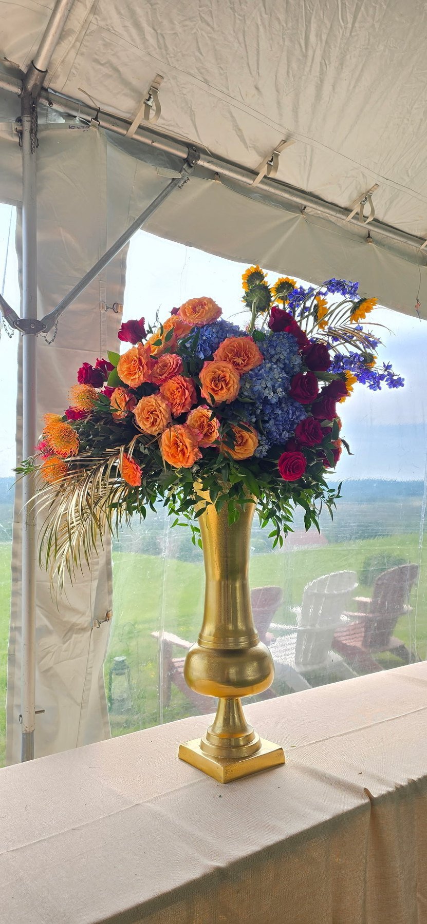 Orange rose arrangement in a tall gold vase