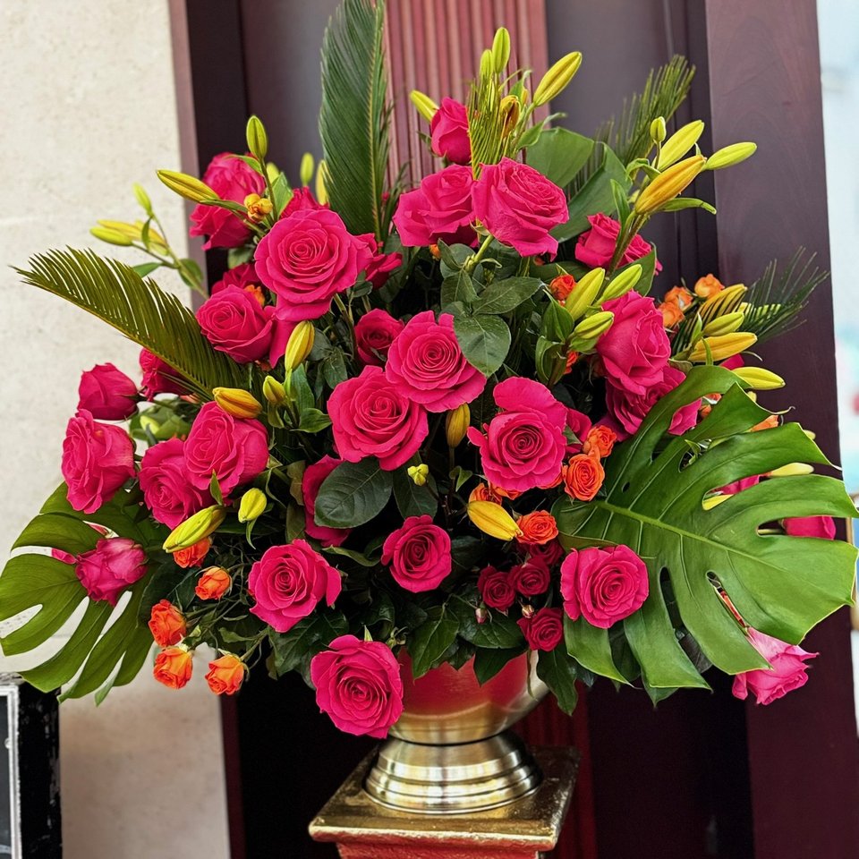 Pink roses and lilies with monstera leaves in a gold urn