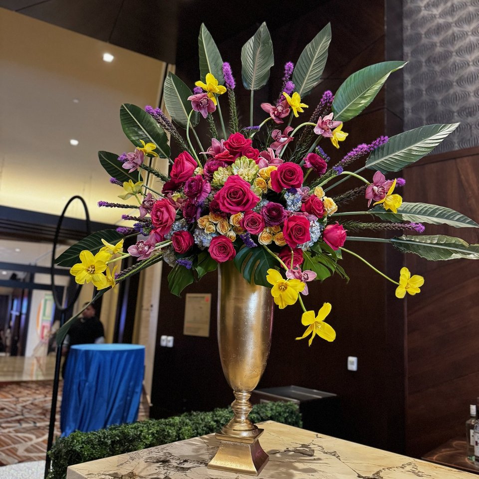 Tropical arrangement with pink roses in a tall gold vase