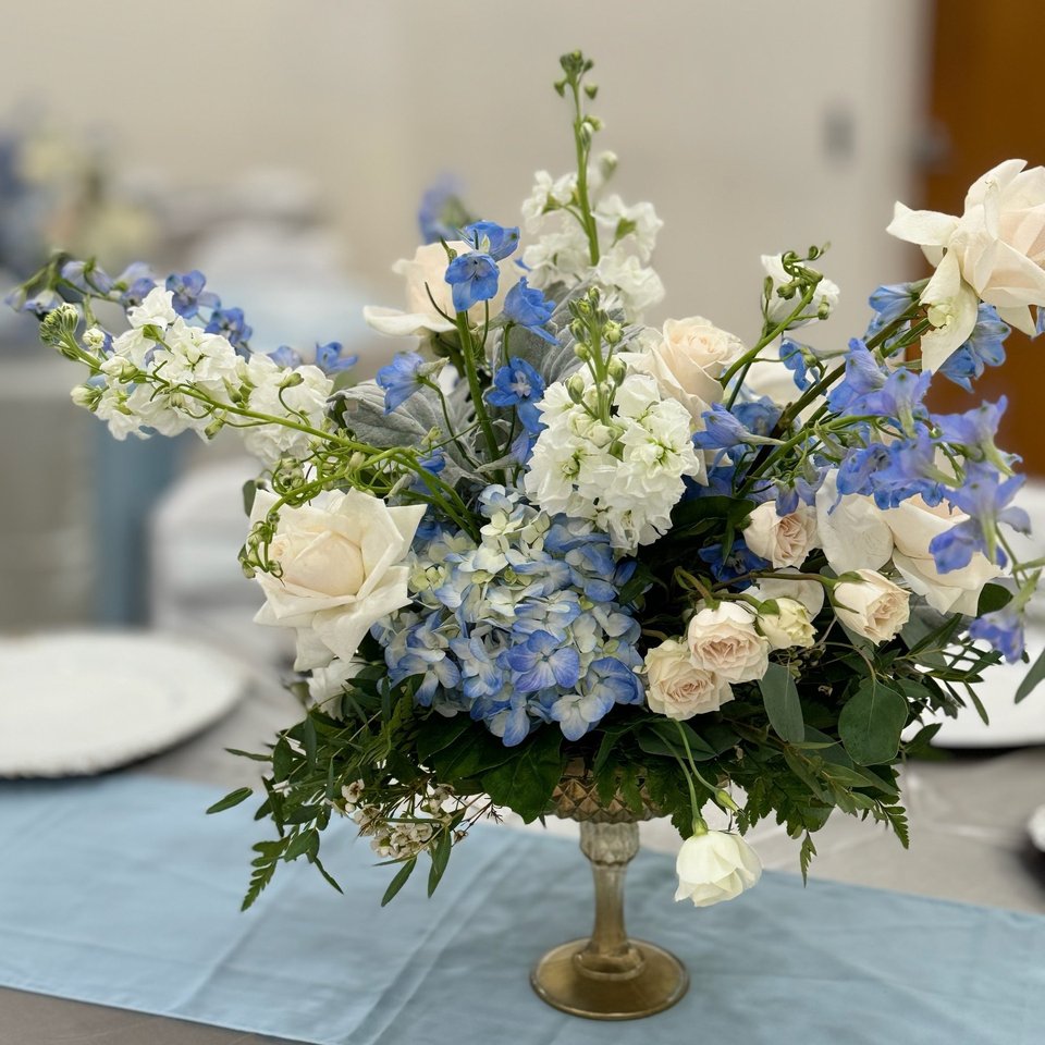 Blue delphinium and white rose arrangement in a gold compote